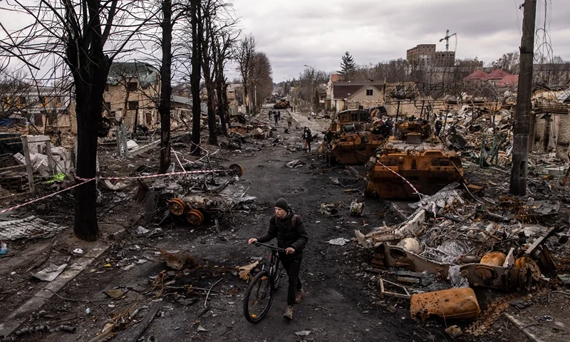 BUCHA, UKRAINE - APRIL 06: A man pushes his bike through debris and destroyed Russian military vehicles on a street on April 06, 2022 in Bucha, Ukraine. The Ukrainian government has accused Russian forces of committing a "deliberate massacre" as they occupied and eventually retreated from Bucha, 25km northwest of Kyiv. Hundreds of bodies have been found in the days since Ukrainian forces regained control of the town. (Photo by Chris McGrath/Getty Images)