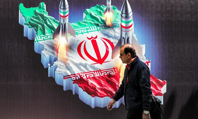 TOPSHOT - A man walks past a banner depicting missiles launching from a representation of the map of Iran coloured with the Iranian flag in central Tehran on April 15, 2024. Iran on April 14 urged Israel not to retaliate militarily to an unprecedented attack overnight, which Tehran presented as a justified response to a deadly strike on its consulate building in Damascus. (Photo by ATTA KENARE / AFP) (Photo by ATTA KENARE/AFP via Getty Images)