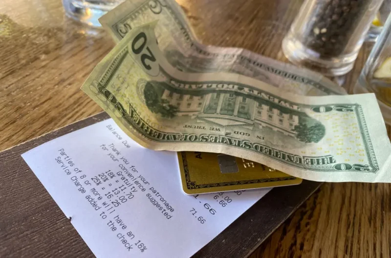 This picture taken on August 24, 2024 shows a bill, with cash for the tip, left on a restaurant table in Los Angeles. Donald Trump and Kamala Harris agree on very little, but the two presidential rivals have found common ground in calling for the elimination of taxes on tips -- a populist move that many criticize as economically irresponsible. Tipping culture in the United States is fundamentally different from most other countries, as customers are encouraged to tip generously on everything from take-out coffee to cocktails. A tip ranging between 15 and 20 percent of the price is considered normal at most restaurants. (Photo by Chris DELMAS / AFP) (Photo by CHRIS DELMAS/AFP via Getty Images)