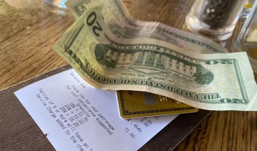This picture taken on August 24, 2024 shows a bill, with cash for the tip, left on a restaurant table in Los Angeles. Donald Trump and Kamala Harris agree on very little, but the two presidential rivals have found common ground in calling for the elimination of taxes on tips -- a populist move that many criticize as economically irresponsible. Tipping culture in the United States is fundamentally different from most other countries, as customers are encouraged to tip generously on everything from take-out coffee to cocktails. A tip ranging between 15 and 20 percent of the price is considered normal at most restaurants. (Photo by Chris DELMAS / AFP) (Photo by CHRIS DELMAS/AFP via Getty Images)