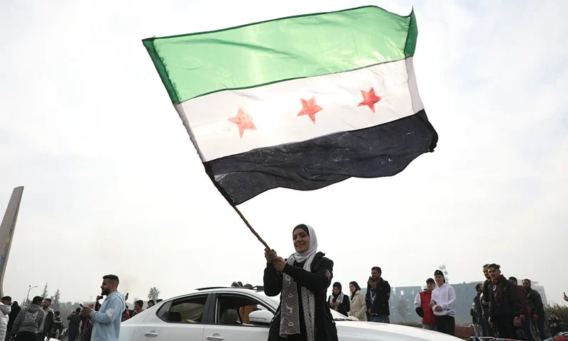 DAMASCUS, SYRIA - DECEMBER 8: A woman waves the flag of the Syrian rebels as people gather to celebrate the fall of the government, in Umayyad Square on December 8, 2024 in Damascus, Syria. Rebel forces in Syria claimed that they had retaken the capital from longtime ruler Bashar al-Assad, who was reported to have fled the country. Syria has been mired in a multi-party civil war since 2011, amid the Arab Spring uprisings. (Photo by Ali Haj Suleiman/Getty Images)