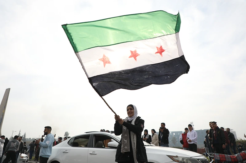 DAMASCUS, SYRIA - DECEMBER 8: A woman waves the flag of the Syrian rebels as people gather to celebrate the fall of the government, in Umayyad Square on December 8, 2024 in Damascus, Syria. Rebel forces in Syria claimed that they had retaken the capital from longtime ruler Bashar al-Assad, who was reported to have fled the country. Syria has been mired in a multi-party civil war since 2011, amid the Arab Spring uprisings. (Photo by Ali Haj Suleiman/Getty Images)