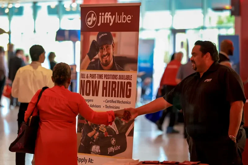 SUNRISE, FLORIDA - APRIL 30: A 'Now Hiring' sign sits next to the Jiffy Lube booth during the Mega JobNewsUSA South Florida Job Fair held in the Amerant Bank Arena on April 30, 2025 in Sunrise, Florida. Over 150 local hiring managers & recruiters were at the job fair to recruit workers for 1000s of positions in Miami, Broward, and Palm Beach County. (Photo by Joe Raedle/Getty Images)