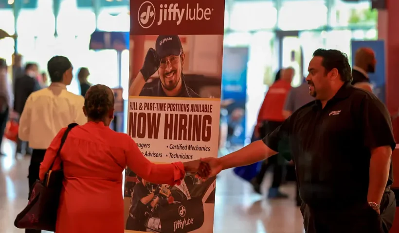 SUNRISE, FLORIDA - APRIL 30: A 'Now Hiring' sign sits next to the Jiffy Lube booth during the Mega JobNewsUSA South Florida Job Fair held in the Amerant Bank Arena on April 30, 2025 in Sunrise, Florida. Over 150 local hiring managers & recruiters were at the job fair to recruit workers for 1000s of positions in Miami, Broward, and Palm Beach County. (Photo by Joe Raedle/Getty Images)