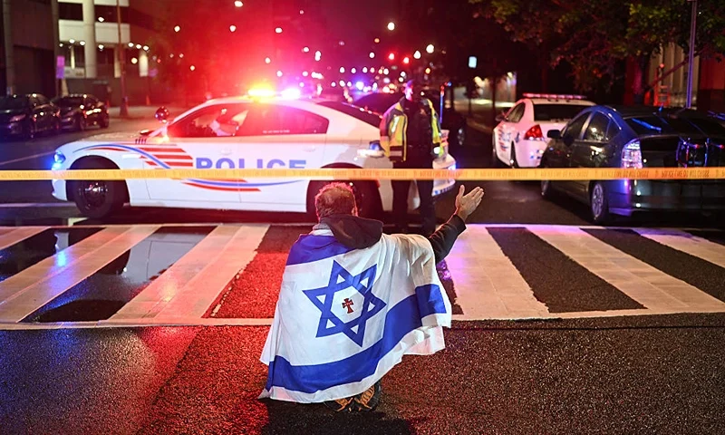 A man draped in the Israeli flag, bearing a cross and the name "Jesus" at its center, gestures as Metropolitan Police officers secure the area outside the Capital Jewish Museum following a shooting that left two people dead in Washington, DC, in the early hours of May 22, 2025. Two Israeli embassy staffers were shot dead late Wednesday, May 21, outside a Jewish museum in Washington by a gunman who shouted "free Palestine," authorities said, with US officials and Israeli diplomats expressing shock and outrage over the killings. (Photo by Alex WROBLEWSKI / AFP) (Photo by ALEX WROBLEWSKI/AFP via Getty Images)