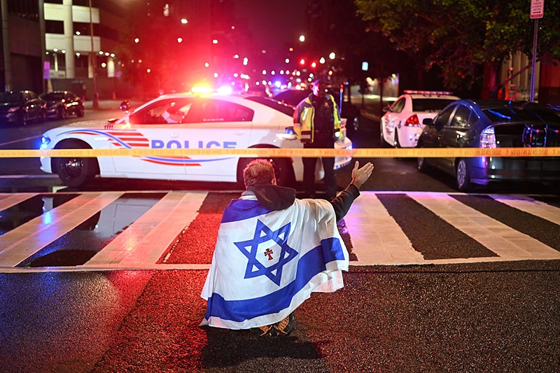A man draped in the Israeli flag, bearing a cross and the name "Jesus" at its center, gestures as Metropolitan Police officers secure the area outside the Capital Jewish Museum following a shooting that left two people dead in Washington, DC, in the early hours of May 22, 2025. Two Israeli embassy staffers were shot dead late Wednesday, May 21, outside a Jewish museum in Washington by a gunman who shouted "free Palestine," authorities said, with US officials and Israeli diplomats expressing shock and outrage over the killings. (Photo by Alex WROBLEWSKI / AFP) (Photo by ALEX WROBLEWSKI/AFP via Getty Images)