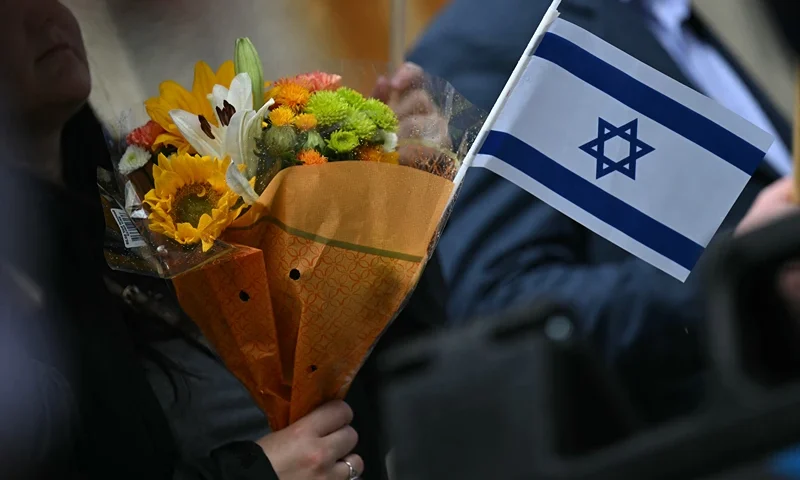 A woman holds flowers and an Israeli national flag in a sign of support outside the Capital Jewish Museum following a shooting that left two people dead, in Washington, DC, on May 22, 2025. Two Israeli embassy staffers, identified as Yaron Lischinsky and Sarah Lynn Milgrim by the Israeli foreign ministry, were shot dead late May 21, outside a Jewish museum in Washington by a gunman who shouted "free Palestine," authorities said, with US officials and Israeli diplomats expressing shock and outrage over the killings. (Photo by Drew ANGERER / AFP) (Photo by DREW ANGERER/AFP via Getty Images)