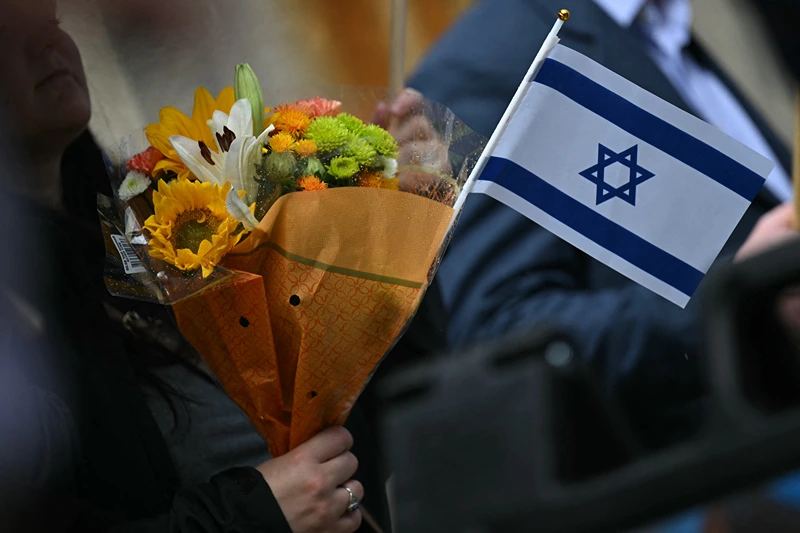 A woman holds flowers and an Israeli national flag in a sign of support outside the Capital Jewish Museum following a shooting that left two people dead, in Washington, DC, on May 22, 2025. Two Israeli embassy staffers, identified as Yaron Lischinsky and Sarah Lynn Milgrim by the Israeli foreign ministry, were shot dead late May 21, outside a Jewish museum in Washington by a gunman who shouted "free Palestine," authorities said, with US officials and Israeli diplomats expressing shock and outrage over the killings. (Photo by Drew ANGERER / AFP) (Photo by DREW ANGERER/AFP via Getty Images)