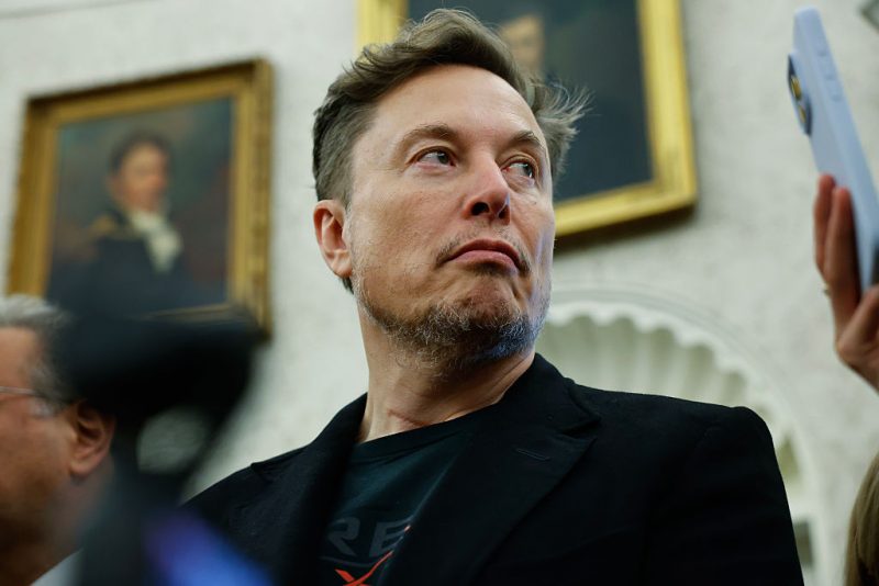 WASHINGTON, DC - MAY 21: Elon Musk listens as reporters ask U.S. President Donald Trump and South Africa President Cyril Ramaphosa questions during a press availability in the Oval Office at the White House on May 21, 2025 in Washington, DC. Relations between the two countries have been strained since Trump signed an executive order in February that claimed white South Africans are the victims of government land confiscation and race-based “genocide,” while admitting some of those Afrikaners as refugees to the United States. Trump also halted all foreign aid to South Africa and expelled the country’s Ambassador to the U.S., Ebrahim Rasool. (Photo by Chip Somodevilla/Getty Images)