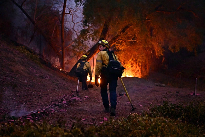 Firefighters work to put out flames in the Mandeville Canyon neighborhood of Los Angeles, California, on January 11, 2025, as the Palisades Fire continues to burn. The Palisades Fire, the largest of the Los Angeles fires, spread toward previously untouched neighborhoods January 11, forcing new evacuations and dimming hopes that the disaster was coming under control. Across the city, at least 16 people have died as multiple fires have ripped through residential areas since January 7, razing thousands of homes in destruction that US President Joe Biden likened to a "war scene." (Photo by AGUSTIN PAULLIER / AFP) (Photo by AGUSTIN PAULLIER/AFP via Getty Images)