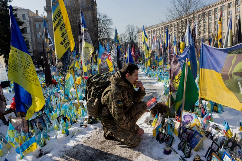 A serviceman kneels down next at a makeshift memorial for the Ukrainian and foreign fighters at Independence Square in Kyiv, on February 24, 2025, during the third anniversary of Russia's invasion of Ukraine. (Photo by Tetiana DZHAFAROVA / AFP) (Photo by TETIANA DZHAFAROVA/AFP via Getty Images)