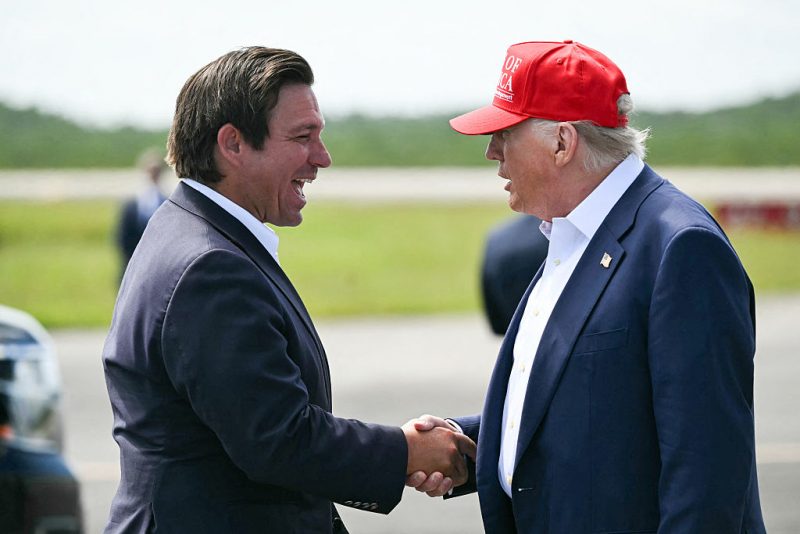 (L/R) Florida Governor Ron DeSantis shakes hands with US President Donald Trump upon Trump's arrival at Dade-Collier Training and Transition Airport in Ochopee, Florida, on July 1, 2025. President Trump is visiting a migrant detention center in a reptile-infested Florida swamp dubbed "Alligator Alcatraz." Trump will attend the opening of the 5,000-bed facility -- located at an abandoned airfield in the Everglades wetlands -- part of his expansion of deportations of undocumented migrants, his spokeswoman said. (Photo by ANDREW CABALLERO-REYNOLDS / AFP) (Photo by ANDREW CABALLERO-REYNOLDS/AFP via Getty Images)
