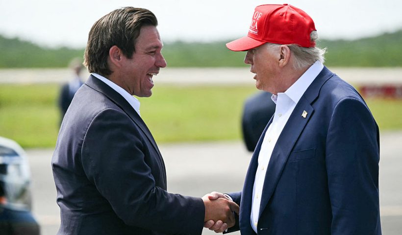 (L/R) Florida Governor Ron DeSantis shakes hands with US President Donald Trump upon Trump's arrival at Dade-Collier Training and Transition Airport in Ochopee, Florida, on July 1, 2025. President Trump is visiting a migrant detention center in a reptile-infested Florida swamp dubbed "Alligator Alcatraz." Trump will attend the opening of the 5,000-bed facility -- located at an abandoned airfield in the Everglades wetlands -- part of his expansion of deportations of undocumented migrants, his spokeswoman said. (Photo by ANDREW CABALLERO-REYNOLDS / AFP) (Photo by ANDREW CABALLERO-REYNOLDS/AFP via Getty Images)