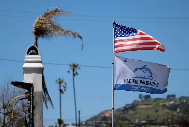 PACIFIC PALISADES, CALIFORNIA - MAY 07: Flags fly over a home destroyed by the Palisades Fire on May 07, 2025 in Pacific Palisades, California. Nearly four months after the Palisades Fire destroyed over 6,800 homes, workers continue to clear hazardous debris from sites where homes had burned, and construction on some new homes has begun. (Photo by Justin Sullivan/Getty Images)