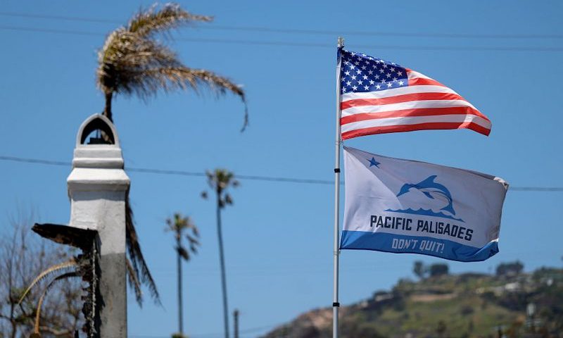 PACIFIC PALISADES, CALIFORNIA - MAY 07: Flags fly over a home destroyed by the Palisades Fire on May 07, 2025 in Pacific Palisades, California. Nearly four months after the Palisades Fire destroyed over 6,800 homes, workers continue to clear hazardous debris from sites where homes had burned, and construction on some new homes has begun. (Photo by Justin Sullivan/Getty Images)