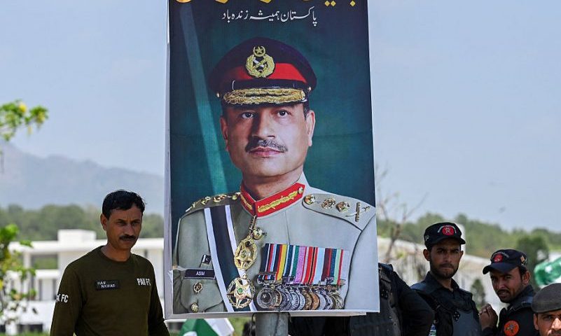 Security personnel stand beside a poster of Pakistani Army Chief General Syed Asim Munir, during a rally to express solidarity with Pakistan's armed forces, in Islamabad on May 14, 2025. The brief conflict between India and Pakistan last week may have left no clear victor, but Islamabad's generals are taking a win, riding a wave of approval on social media to burnish their recently tarnished image. (Photo by Aamir QURESHI / AFP) (Photo by AAMIR QURESHI/AFP via Getty Images)