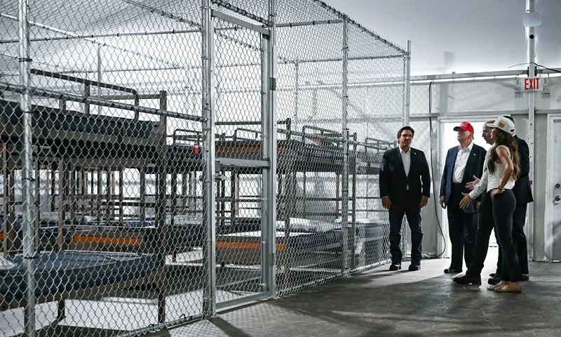 TOPSHOT - US President President Donald Trump (2L), Florida Governor Ron DeSantis (L), and Secretary of Homeland Security Kristi Noem (R) tour a migrant detention center, dubbed "Alligator Alcatraz," located at the site of the Dade-Collier Training and Transition Airport in Ochopee, Florida on July 1, 2025. President Trump is visiting a migrant detention center in a reptile-infested Florida swamp dubbed "Alligator Alcatraz." Trump will attend the opening of the 5,000-bed facility -- located at an abandoned airfield in the Everglades wetlands -- part of his expansion of deportations of undocumented migrants, his spokeswoman said. (Photo by ANDREW CABALLERO-REYNOLDS / AFP) (Photo by ANDREW CABALLERO-REYNOLDS/AFP via Getty Images)