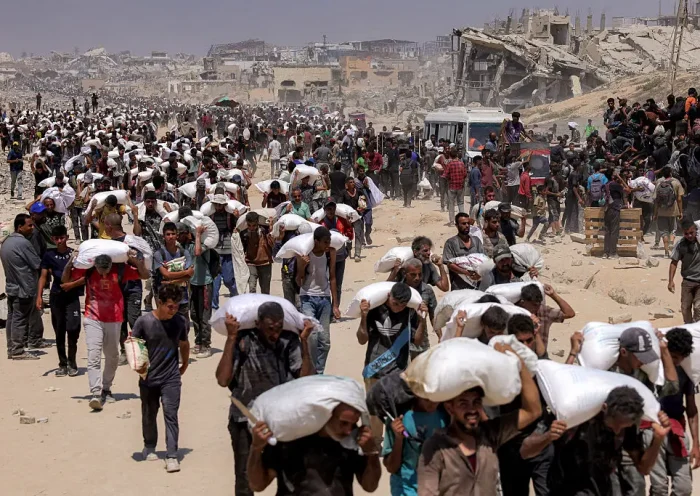 TOPSHOT - People walk with sacks of flour delivered after trucks carrying humanitarian aid entered northern Gaza on July 27, 2025 coming from the Zikim border crossing. (Photo by BASHAR TALEB / AFP) (Photo by BASHAR TALEB/AFP via Getty Images)