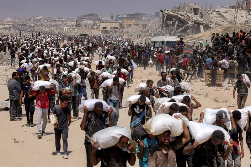 TOPSHOT - People walk with sacks of flour delivered after trucks carrying humanitarian aid entered northern Gaza on July 27, 2025 coming from the Zikim border crossing. (Photo by BASHAR TALEB / AFP) (Photo by BASHAR TALEB/AFP via Getty Images)