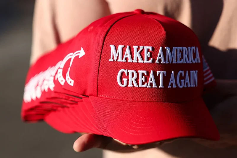 A member of Turning Point USA distributes MAGA hats to people gathered at a makeshift memorial for right-wing activist and Turning Point USA founder Charlie Kirk outside of their headquarters in Phoenix, Arizona, on September 19, 2025. The widow of slain right-wing activist Charlie Kirk is to take his place at the head of youth action campaign group Turning Point USA, officials announced on September 18. Two days after her husband was shot dead on a univerity campus, allegedly by a 22-year-old gunman, Erika Kirk told supporters: "The movement my husband built will not die." (Photo by CHARLY TRIBALLEAU / AFP) (Photo by CHARLY TRIBALLEAU/AFP via Getty Images)