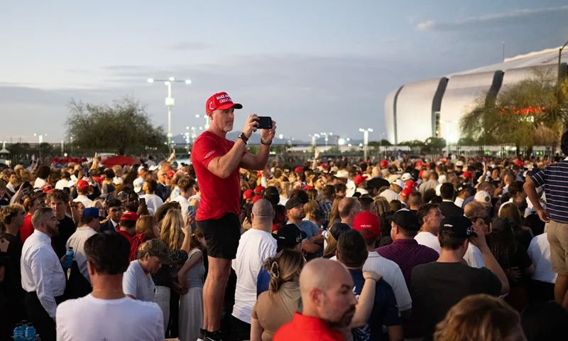 A man wearing a MAGA hat holds his phone as people arrive to attend the public memorial service of right-wing activist Charlie Kirk outside State Farm stadium in Glendale, Arizona, on September 21, 2025. (Photo by ANDREW CABALLERO-REYNOLDS / AFP) (Photo by ANDREW CABALLERO-REYNOLDS/AFP via Getty Images)