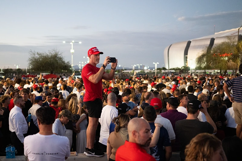 A man wearing a MAGA hat holds his phone as people arrive to attend the public memorial service of right-wing activist Charlie Kirk outside State Farm stadium in Glendale, Arizona, on September 21, 2025. (Photo by ANDREW CABALLERO-REYNOLDS / AFP) (Photo by ANDREW CABALLERO-REYNOLDS/AFP via Getty Images)