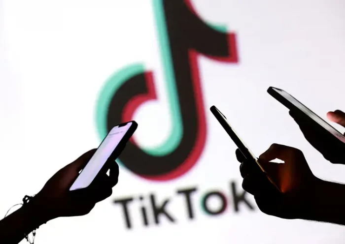 Teenagers pose for a photo while holding smartphones in front of a TikTok logo in this illustration taken September 11, 2025. REUTERS/Dado Ruvic/Illustration/File Photo