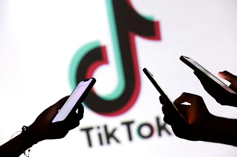Teenagers pose for a photo while holding smartphones in front of a TikTok logo in this illustration taken September 11, 2025. REUTERS/Dado Ruvic/Illustration/File Photo
