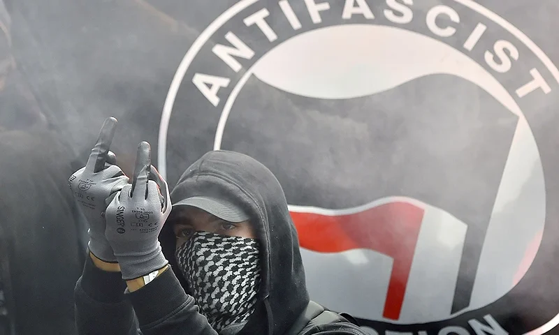 TOPSHOT - A demonstrator gestures in front of an Antifascist Action flag during a demonstration against the controversial labour reforms of the French government in Nantes, western France, on September 15, 2016. - Opponents of France's controversial labour reforms took to the streets on September 15, 2016 for the 14th time in six months in a last-ditch bid to quash the measures that lost the Socialist government crucial support on the left. (Photo by LOIC VENANCE / AFP) (Photo by LOIC VENANCE/AFP via Getty Images)