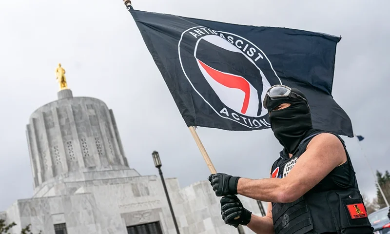 SALEM, OR - MARCH 28: A protester waves an anti-fascist flag at the Oregon statehouse on March 28, 2021 in Salem, Oregon. The protesters clashed with occupants of vehicles that had participated in an American flag-waving car caravan, despite law enforcements efforts to to keep the groups separate. (Photo by Nathan Howard/Getty Images)