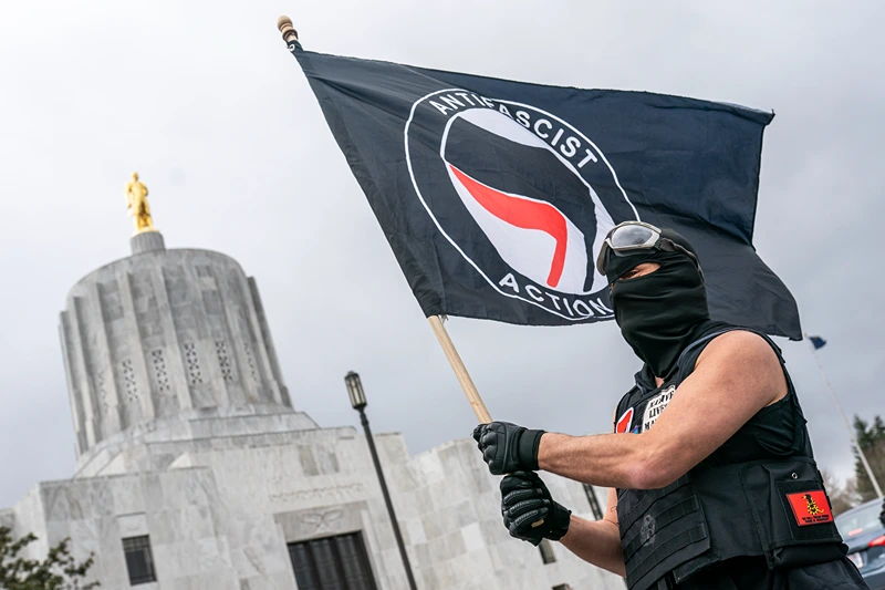SALEM, OR - MARCH 28: A protester waves an anti-fascist flag at the Oregon statehouse on March 28, 2021 in Salem, Oregon. The protesters clashed with occupants of vehicles that had participated in an American flag-waving car caravan, despite law enforcements efforts to to keep the groups separate. (Photo by Nathan Howard/Getty Images)