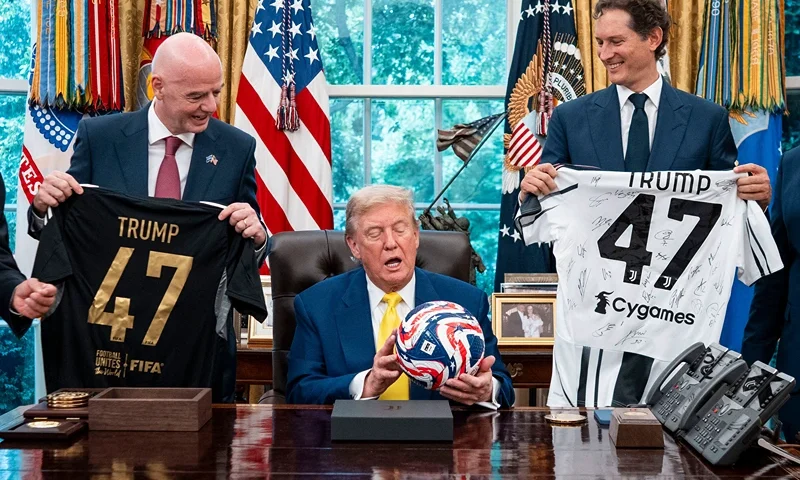 US President Donald Trump (C), flanked by Chairperson of Ferrari John Elkann (R) and FIFA President Gianni Infantino, holds a ball as he makes remarks in the Oval Office of the White House during a visit by members of Italian soccer club Juventus in Washington, DC, on June 18, 2025. Juventus will play Emirati club Al-Ain in the 2025 FIFA Club World Cup at Washington's Audi Field later in the day. (Photo by Doug Mills / POOL / AFP) / ALTERNATE CROP (Photo by DOUG MILLS/POOL/AFP via Getty Images)
