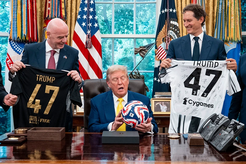 US President Donald Trump (C), flanked by Chairperson of Ferrari John Elkann (R) and FIFA President Gianni Infantino, holds a ball as he makes remarks in the Oval Office of the White House during a visit by members of Italian soccer club Juventus in Washington, DC, on June 18, 2025. Juventus will play Emirati club Al-Ain in the 2025 FIFA Club World Cup at Washington's Audi Field later in the day. (Photo by Doug Mills / POOL / AFP) / ALTERNATE CROP (Photo by DOUG MILLS/POOL/AFP via Getty Images)