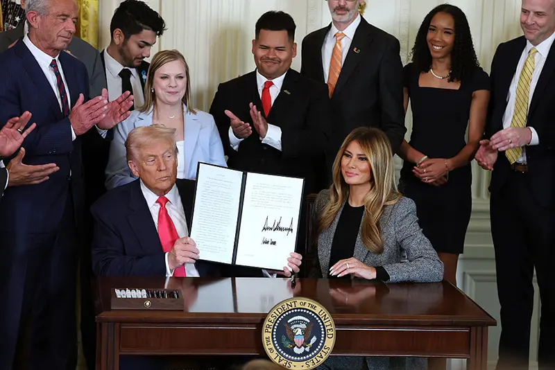 U.S. President Donald Trump, joined by first lady Melania Trump, members of his administration and foster care advocates, holds up a copy of the "Fostering the Future" executive order after signing the order in the East Room of the White House on November 13, 2025 in Washington, DC. (Photo by Anna Moneymaker/Getty Images)