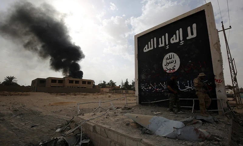 Iraqi fighters of the Hashed al-Shaabi (Popular Mobilisation units) stand next to a wall bearing the Islamic State (IS) group flag as they enter the city of al-Qaim, in Iraq's western Anbar province near the Syrian border as they fight against remnant pockets of Islamic State group jihadists on November 3, 2017. (Photo by AHMAD AL-RUBAYE / AFP) (Photo by AHMAD AL-RUBAYE/AFP via Getty Images)