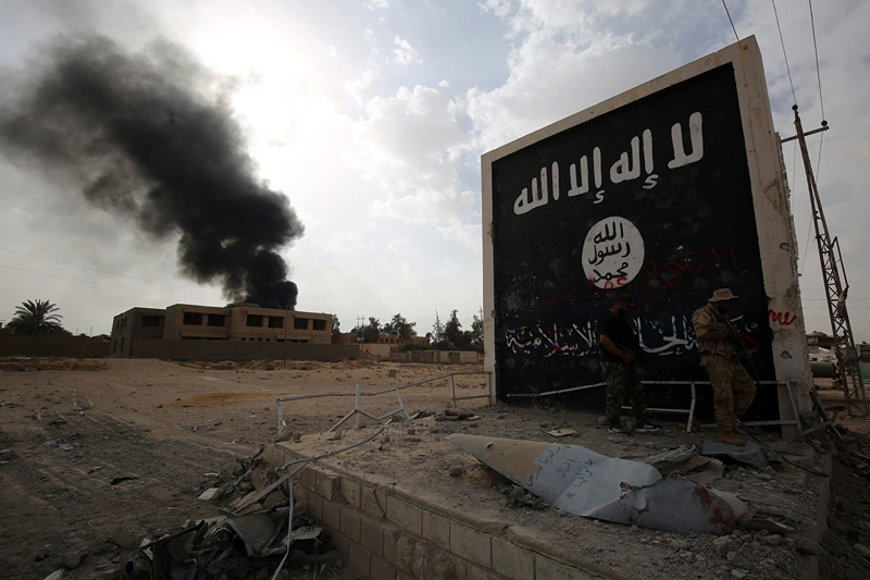 Iraqi fighters of the Hashed al-Shaabi (Popular Mobilisation units) stand next to a wall bearing the Islamic State (IS) group flag as they enter the city of al-Qaim, in Iraq's western Anbar province near the Syrian border as they fight against remnant pockets of Islamic State group jihadists on November 3, 2017. (Photo by AHMAD AL-RUBAYE / AFP) (Photo by AHMAD AL-RUBAYE/AFP via Getty Images)