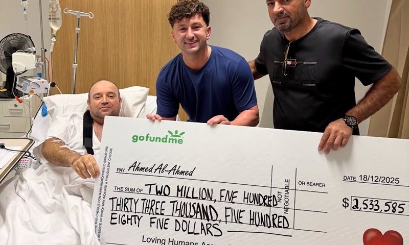 A picture shared to X shows Zachery Dereniowski (M) handing Ahmed al Ahmed (R) a check of $2,544,585 AUS, about $1.6 million USD, while he recovers in a hospital bed. (Photo: 6ixbuzztv via X)