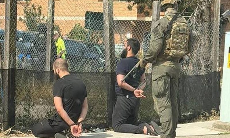 In a photograph shared on X, two men are seen detained with zipties as Armed Australian SWAT members loom behind them. (Photo: NDTV WORLD Via X)