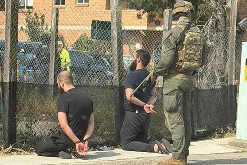 In a photograph shared on X, two men are seen detained with zipties as Armed Australian SWAT members loom behind them. (Photo: NDTV WORLD Via X)