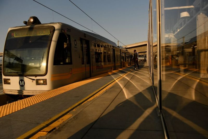 Transit passengers wear face masks as they wait to board the Metro C Line, formerly Green Line, light rail train alongside the 105 Freeway at the Judge Harry Pregerson Interchange during rush hour traffic in Los Angeles, California on July 16, 2021. - The Metro C Line will eventually merge with the Crenshaw/LAX Transit Project as infrastructure modernization and transit construction projects continue at the airport ahead of the 2028 Los Angeles Olympics to reduce carbon emissions, traffic, and their impact towards climate change. (Photo by Patrick T. FALLON / AFP) (Photo by PATRICK T. FALLON/AFP via Getty Images)