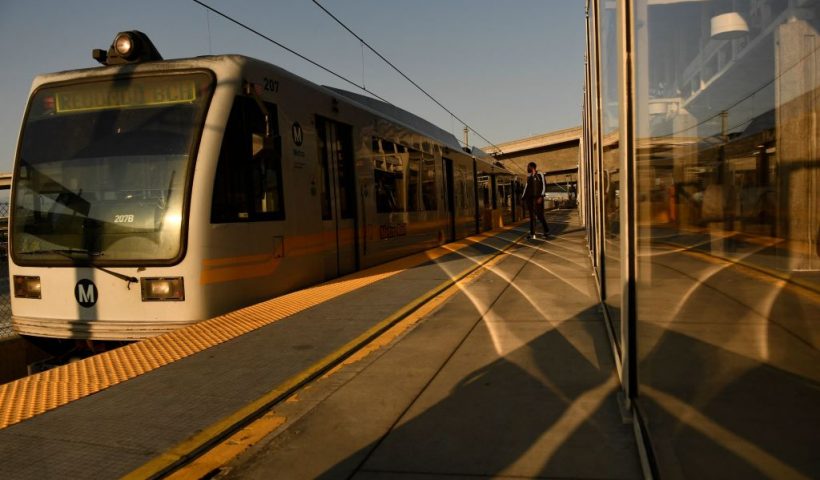 Transit passengers wear face masks as they wait to board the Metro C Line, formerly Green Line, light rail train alongside the 105 Freeway at the Judge Harry Pregerson Interchange during rush hour traffic in Los Angeles, California on July 16, 2021. - The Metro C Line will eventually merge with the Crenshaw/LAX Transit Project as infrastructure modernization and transit construction projects continue at the airport ahead of the 2028 Los Angeles Olympics to reduce carbon emissions, traffic, and their impact towards climate change. (Photo by Patrick T. FALLON / AFP) (Photo by PATRICK T. FALLON/AFP via Getty Images)