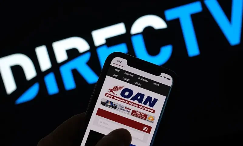 This illustration photo shows a person reading the One America Network website on a smartphone in front of a DirecTV logo. (Photo by Chris DELMAS / AFP) (Photo by CHRIS DELMAS/AFP via Getty Images)