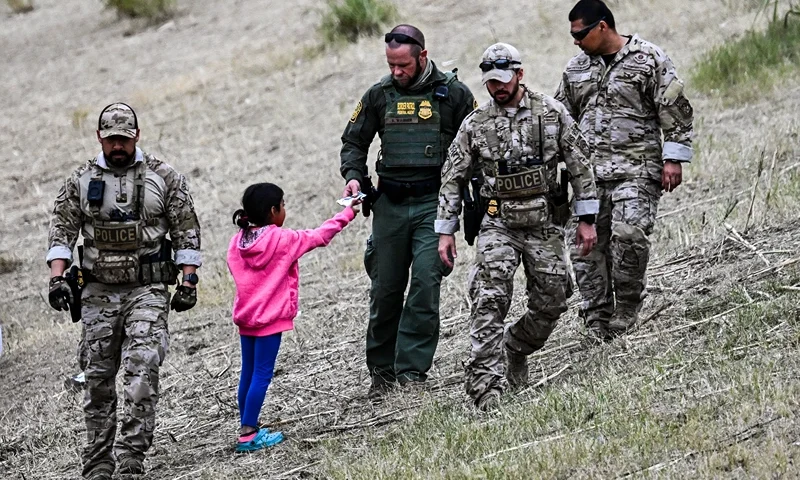 TOPSHOT - A US Customs and Border Protection officer gives food to an immigrant child waiting to be processed at a US Border Patrol transit center after crossing the border from Mexico at Eagle Pass, Texas on December 22, 2023. Texas Republican Governor Greg Abbott signed a bill on December 18, 2023 that would allow state police to arrest and deport migrants who cross illegally into the US from Mexico. (Photo by CHANDAN KHANNA / AFP) (Photo by CHANDAN KHANNA/AFP via Getty Images)