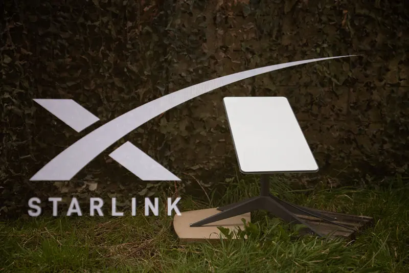 Double exposure photograph of the starlink logo and satellite antenna on the ground in front of a military camouflage net in Kerlouan in Brittany in France on March 01 2025. (Photo by Vincent Feuray / Hans Lucas / Hans Lucas via AFP) (Photo by VINCENT FEURAY/Hans Lucas/AFP via Getty Images)