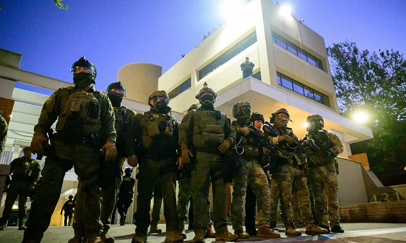 Federal agents, including members of the Department of Homeland Security, Border Patrol, and others, stand guard outside an Immigration and Customs Enforcement (ICE) facility in downtown Portland, Oregon, on October 6, 2025. President Donald Trump threatened on October 6, 2025, to use emergency powers against rebellion to deploy more troops into Democratic-led US cities, intensifying his rhetoric as his attempts to mobilize the military face legal challenges. Trump openly mulled use of the Insurrection Act after a federal judge in Oregon temporarily halted a National Guard deployment in Portland, while another judge in Illinois allowed a similar move to proceed for now in Chicago. (Photo by Mathieu Lewis-Rolland / AFP) (Photo by MATHIEU LEWIS-ROLLAND/AFP via Getty Images)