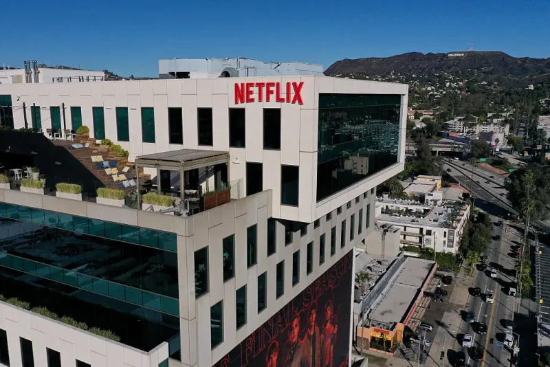 This aerial picture taken on December 5, 2025, shows the Netflix logo above Hollywood studio offices at Sunset Bronson Studios as the Hollywood sign stands on the horizon in Los Angeles, California. Streaming giant Netflix said December 5, 2025 it will buy film and television studio Warner Bros. Discovery for nearly $83 billion, the entertainment industry's biggest consolidation deal this decade. The acquisition gives Netflix access to a vast film catalog as well as the prestigious streaming service HBO Max. (Photo by Patrick T. Fallon / AFP via Getty Images)