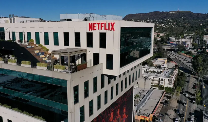 This aerial picture taken on December 5, 2025, shows the Netflix logo above Hollywood studio offices at Sunset Bronson Studios as the Hollywood sign stands on the horizon in Los Angeles, California. Streaming giant Netflix said December 5, 2025 it will buy film and television studio Warner Bros. Discovery for nearly $83 billion, the entertainment industry's biggest consolidation deal this decade. The acquisition gives Netflix access to a vast film catalog as well as the prestigious streaming service HBO Max. (Photo by Patrick T. Fallon / AFP via Getty Images)