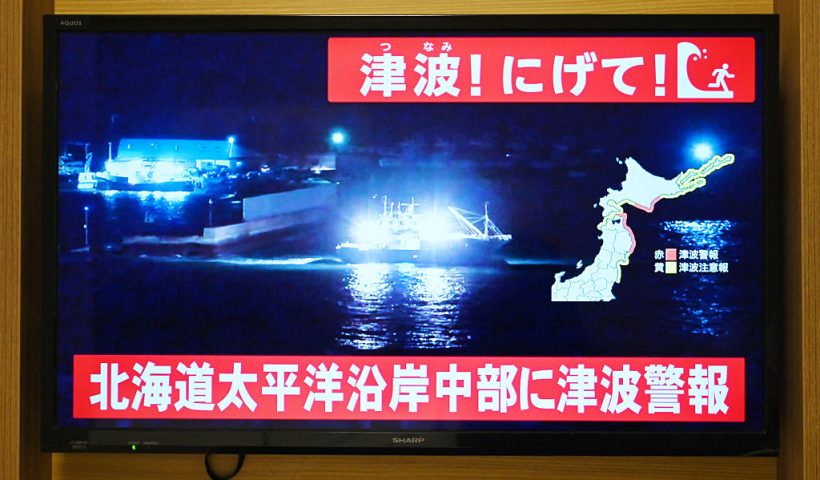 TOPSHOT - An advisory reading "Tsunami! Run!" (top) and "Tsunami warning issued for central Hokkaido's Pacific Coast" flashes over the live footage of a boat leaving a port, on a television screen in Sapporo, in Japan's northern Hokkaido prefecture on December 8, 2025. Japan recorded a 40-centimetre (16-inch) tsunami after a 7.6-magnitude quake on December 8. (Photo by GREG BAKER / AFP via Getty Images)