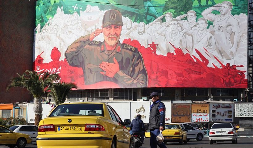 Iranians ride their motorbike past a huge banner of former Iran Islamic Revolutionary Guard Corps (IRGC) Quds Force commander Qasem Soleimani ahead of the sixth anniversary of his assassination Iraq, at Valiasr Square in Tehran, on December 31, 2025. Soleimani was killed on January 3, 2020, in a targeted US airstrike at Baghdad airport in Iraq. (Photo by ATTA KENARE / AFP via Getty Images)