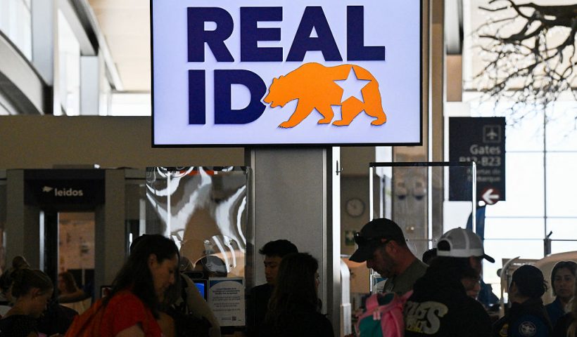 Travelers wait in line to pass through security and TSA screen under a sign reading "REAL ID" at Sacramento International Airport on May 15, 2025 in Sacramento, California. Real ID is a federally mandated form of identification in the US that meets enhanced security standards set by the Department of Homeland Security. Starting May 7, 2025, US residents will need a Real ID-compliant driver's license or identification card (or an acceptable alternative like a passport) to board domestic flights and enter certain federal facilities. (Photo by Robyn Beck / AFP) (Photo by ROBYN BECK/AFP via Getty Images)
